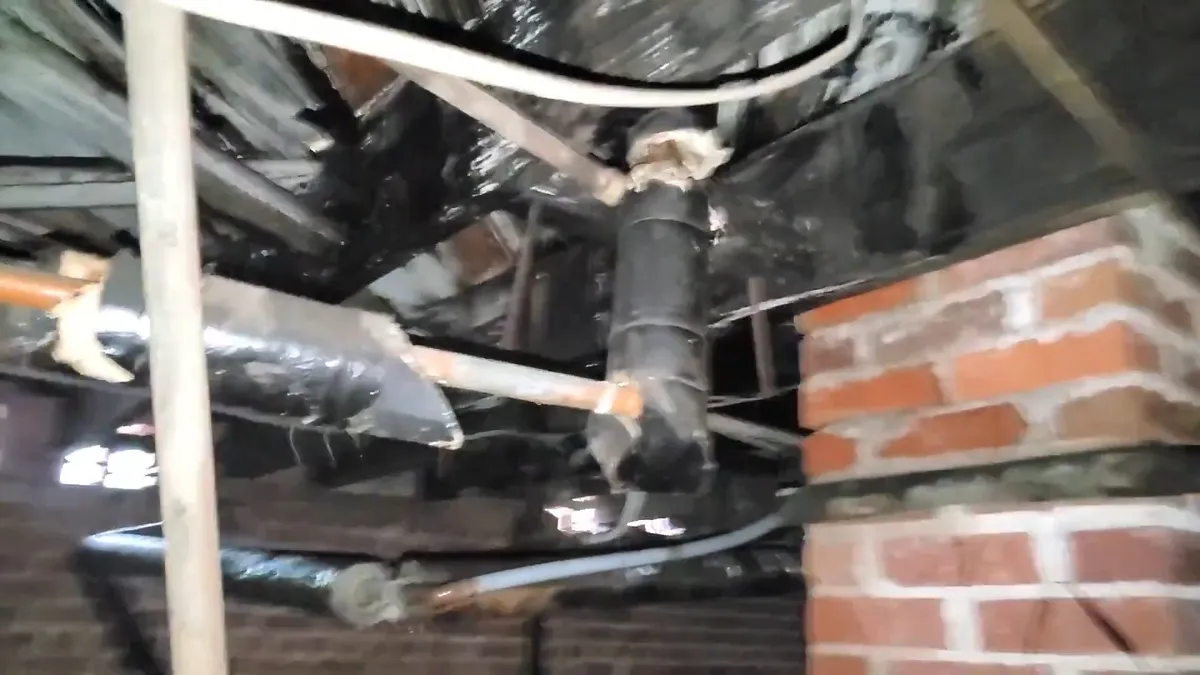 Multiple drain and supply lines run through a brick-walled crawlspace for Maricopa Plumbing Pros